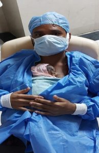Man in full PPE provides KMC to a small newborn.