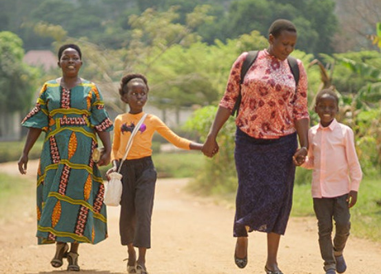 Two women and two children, a boy and a girl, walk down a dirt road hand in hand