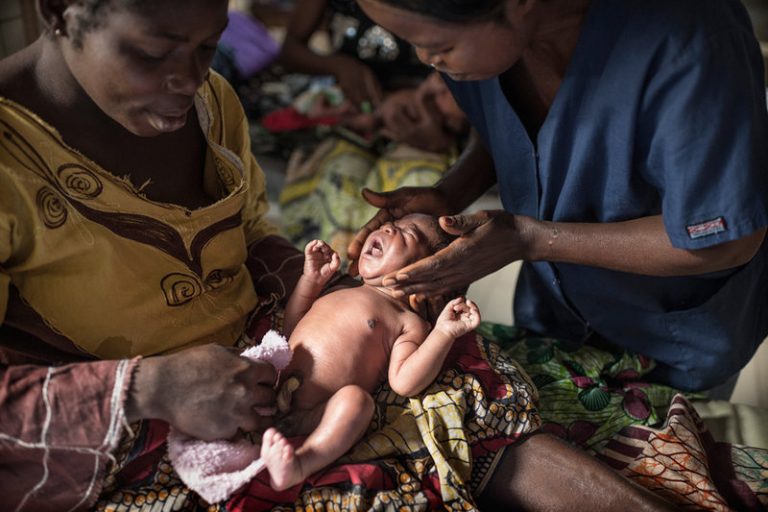 Photo of a health worker providing umbilical cord care to a newborn while the mother watches.